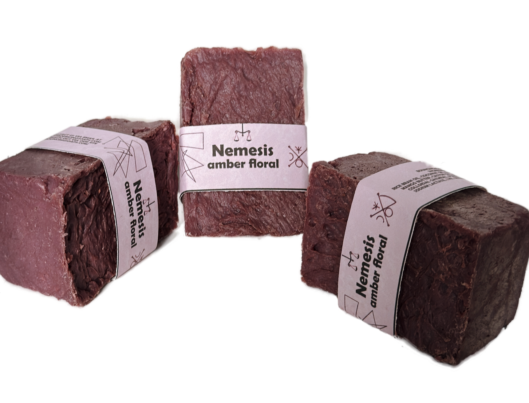 Three Nemesis soap bars arranged in a triangular grouping on a white background, showing the rich maroon color and lavender label from multiple angles