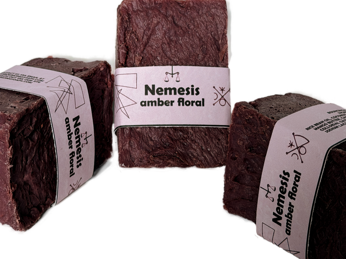 Three Nemesis soap bars arranged in a triangular grouping on a white background, showing the rich maroon color and lavender label from multiple angles