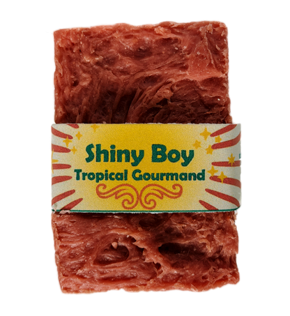 Coral-rose handmade soap bar with swirled rustic texture, wrapped in a vintage carnival-style yellow and cream band reading "Shiny Boy – Tropical Gourmand"