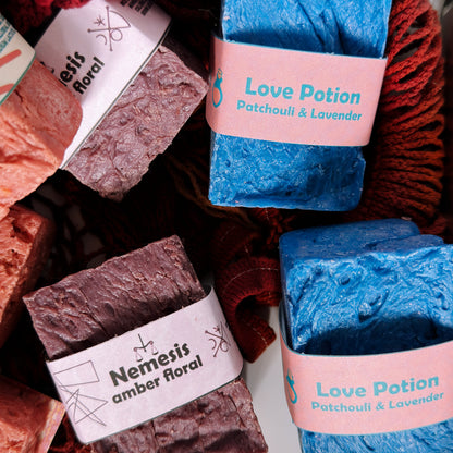 Assorted Bouncing Soaps handmade bar soaps in a red rope basket including blue Love Potion Patchouli and Lavender and purple Nemesis Amber Floral