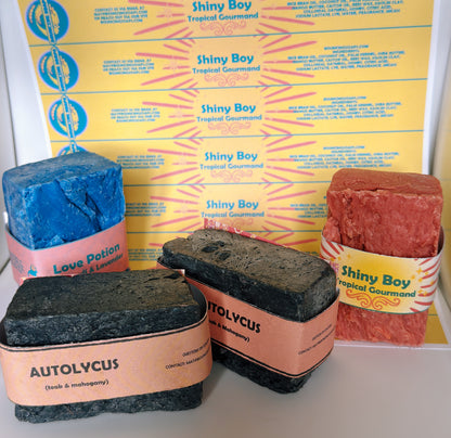 Four soap bars with colorful packaging in front of a yellow box labeled 'Shiny Boy'.
